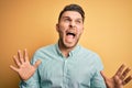 Young business man with blue eyes wearing elegant green shirt over yellow background crazy and mad shouting and yelling with Royalty Free Stock Photo