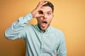 Young business man with blue eyes wearing elegant green shirt over yellow background doing ok gesture shocked with surprised face, Royalty Free Stock Photo