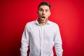 Young business man with blue eyes wearing elegant shirt standing over red isolated background afraid and shocked with surprise and Royalty Free Stock Photo