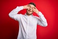 Young business man with blue eyes wearing elegant shirt standing over red isolated background covering eyes with hands smiling Royalty Free Stock Photo