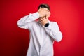 Young business man with blue eyes wearing elegant shirt standing over red isolated background Covering eyes and mouth with hands, Royalty Free Stock Photo