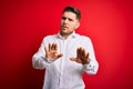 Young business man with blue eyes wearing elegant shirt standing over red isolated background Moving away hands palms showing Royalty Free Stock Photo