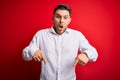 Young business man with blue eyes wearing elegant shirt standing over red isolated background Pointing down with fingers showing Royalty Free Stock Photo