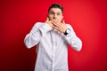 Young business man with blue eyes wearing elegant shirt standing over red isolated background shocked covering mouth with hands Royalty Free Stock Photo