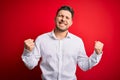 Young business man with blue eyes wearing elegant shirt standing over red isolated background very happy and excited doing winner Royalty Free Stock Photo