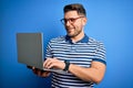 Young business man with blue eyes wearing glasses working using computer laptop with a happy face standing and smiling with a Royalty Free Stock Photo