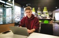 Young business man in casual clothes, and sitting at a table in a fast food cafe, uses a laptop Royalty Free Stock Photo