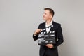Young business man in classic black suit looking aside holding classic black film making clapperboard isolated on grey Royalty Free Stock Photo