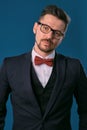 Young business man in classic black suit, white shirt, red bow-tie and glasses. Posing against blue studio background Royalty Free Stock Photo