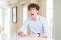 Young business man with curly read head angry and mad screaming frustrated and furious, shouting with anger