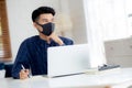 Young business man in face mask planning and working from home on laptop computer on desk. Royalty Free Stock Photo