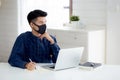 Young business man in face mask planning and working from home on laptop computer on desk. Royalty Free Stock Photo