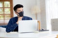 Young business man in face mask planning and working from home on laptop computer. Royalty Free Stock Photo