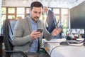 Young business man in formal wear using mobile phone and holding eyeglasses in other hand while sitting at his workplace Royalty Free Stock Photo