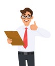 Young business man holding clipboard and showing thumbs up sign. Trendy person keeping notepad, document or folder. Male character