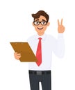 Young  business man holding clipboard and showing victory, peace or two sign with fingers. Person keeping notepad, document. Royalty Free Stock Photo