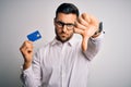 Young business man holding credit card over isolated background with angry face, negative sign showing dislike with thumbs down, Royalty Free Stock Photo