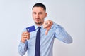 Young business man holding credit card over isolated background with angry face, negative sign showing dislike with thumbs down, Royalty Free Stock Photo