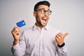 Young business man holding credit card over isolated background pointing and showing with thumb up to the side with happy face Royalty Free Stock Photo