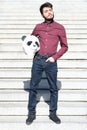 Young business man with a panda head mask in his hands, standing on stairs