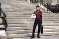 Young business man with a panda head mask in his hands and a suitcase, standing on stairs