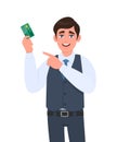 Young business man showing credit, debit card and pointing finger hand. Trendy person in waistcoat holding ATM card. Royalty Free Stock Photo