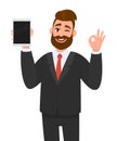 Young business man showing/holding blank screen of tablet computer display and gesturing/making okay, ok sign, while winking eye. Royalty Free Stock Photo