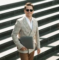 Handsome smiling young business man spending time outdoors at the city, using laptop computer on stairs Royalty Free Stock Photo