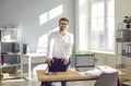 Young business man standing near his workplace at office, looking at the camera and smiling. Royalty Free Stock Photo