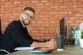 Young business man is using laptop while sitting in the office, looking at camera, smiling Royalty Free Stock Photo