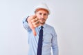 Young business man wearing contractor safety helmet over isolated background looking unhappy and angry showing rejection and Royalty Free Stock Photo