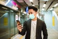 Young business man wearing face mask watching mobile phone and waiting for the train