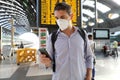 Young business man wearing KN95 FFP2 face mask at train station. Young caucasian man with behind timetables of departures arrivals