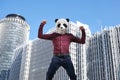 Young business man wearing a panda head mask, strong in front of the corporate buildings