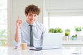 Young business man working with computer laptop at the office surprised with an idea or question pointing finger with happy face, Royalty Free Stock Photo