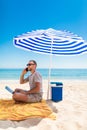 Young business man working with computer and talking on smartphone under solar umbrella on Sandy beach, blue sea and sky Royalty Free Stock Photo