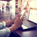 young business man working on his laptop and using smart phone sitting at wooden table in a coffee shop Royalty Free Stock Photo