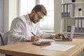 Young business man working with laptop computer at home or at office and writing. Royalty Free Stock Photo