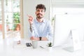 Young business man working using computer with a big smile on face, pointing with hand and finger to the side looking at the Royalty Free Stock Photo