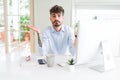 Young business man working using computer clueless and confused expression with arms and hands raised Royalty Free Stock Photo