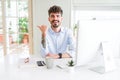 Young business man working using computer smiling with happy face looking and pointing to the side with thumb up Royalty Free Stock Photo