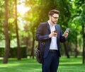 Young business manager with takeout coffee browsing net on cellphone at city park