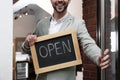 Young business owner holding sign OPEN at door of cafe, closeup