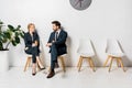 young business people holding paper cups and looking at each other while waiting on chairs Royalty Free Stock Photo