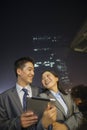 Young business people smiling and holding digital tablet, night and outdoors