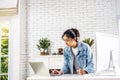 Young business smiling happy asian woman working on a laptop and writing down ideas in a paperwork at home, work from home concept Royalty Free Stock Photo