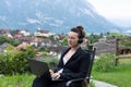 A young business woman in a black suit works on a laptop on the background of mountains. Home office