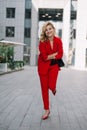 Young business woman blonde in a red suit is walking outdoors in the courtyard of a business center. Stylish people. Soft