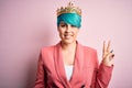 Young business woman with blue fashion hair wearing queen crown over pink isolated background smiling with happy face winking at Royalty Free Stock Photo