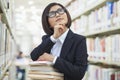 Young Business Woman Contemplating and Looking Up in Bookstore with a Stack of Books